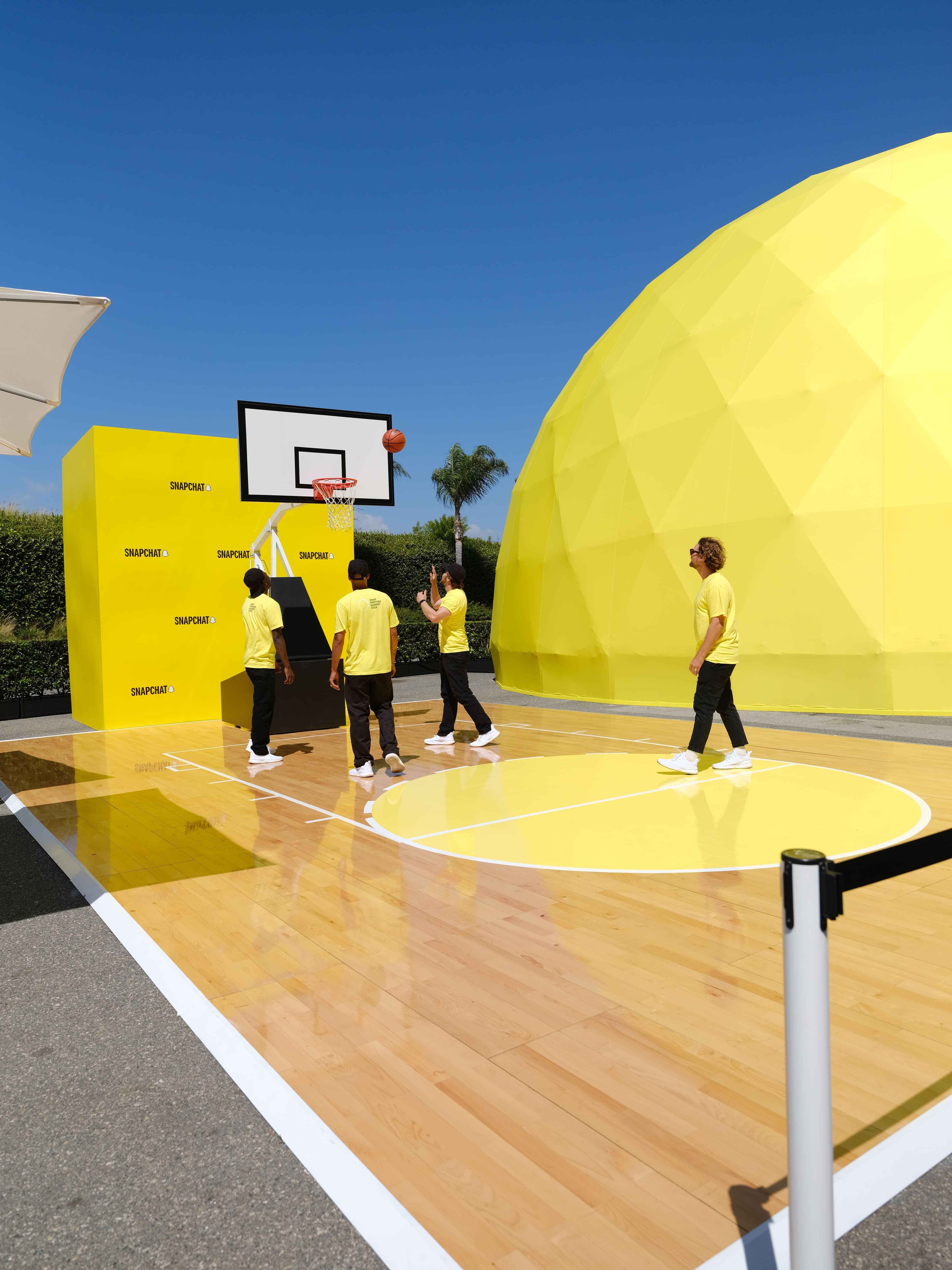 Yellow geodesic dome on an outdoor basketball court with people walking past.