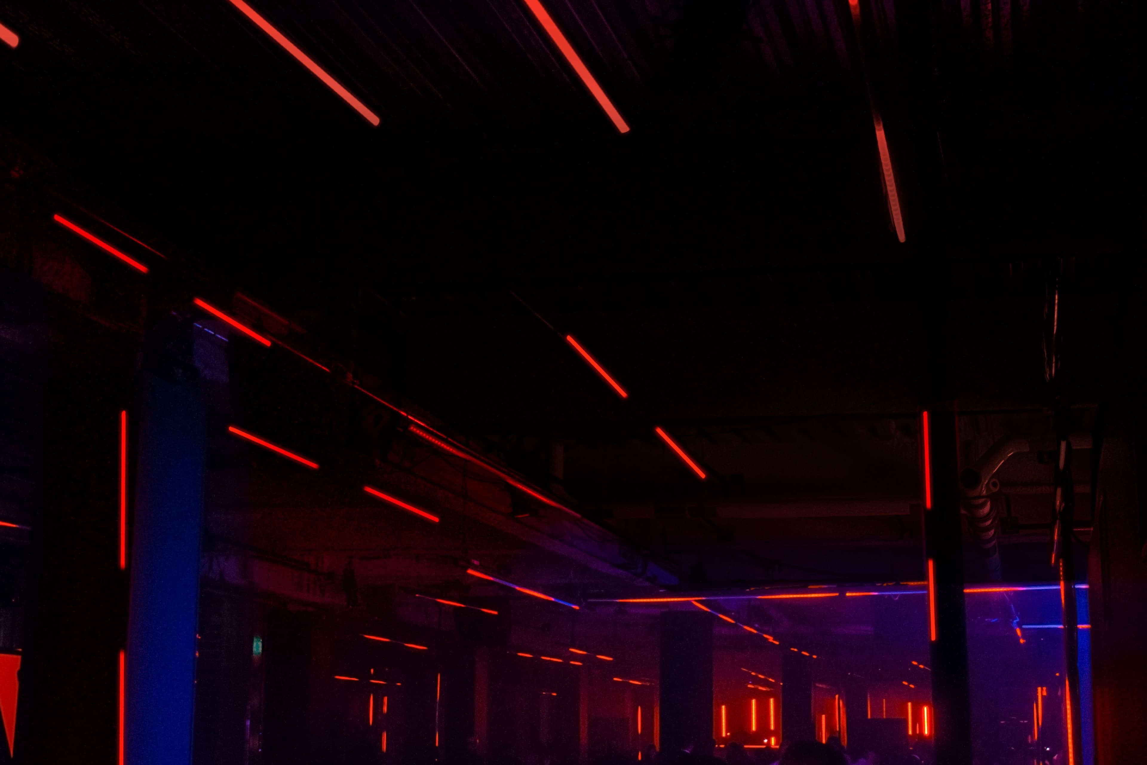 Dark ceiling with crossing red neon light beams above a moody industrial-style space.