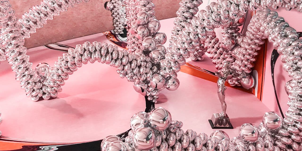 Tangled silver spiral bead sculptures arranged on a pink stage with a small trophy in the background