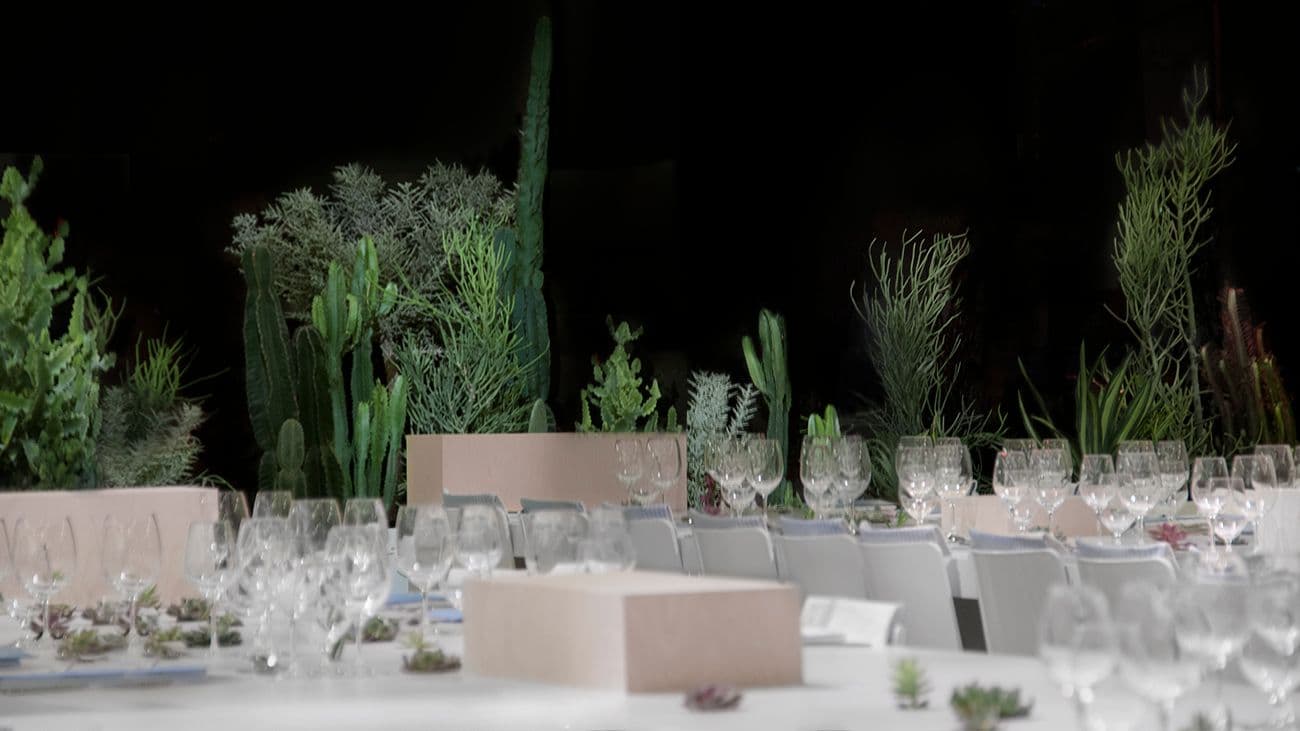 Dark, candlelit dinner table lined with tall cactus and greenery centerpieces
