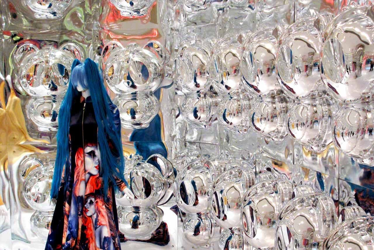 Colorful mirrored disco-ball sculptures with clothing hanging in the background.