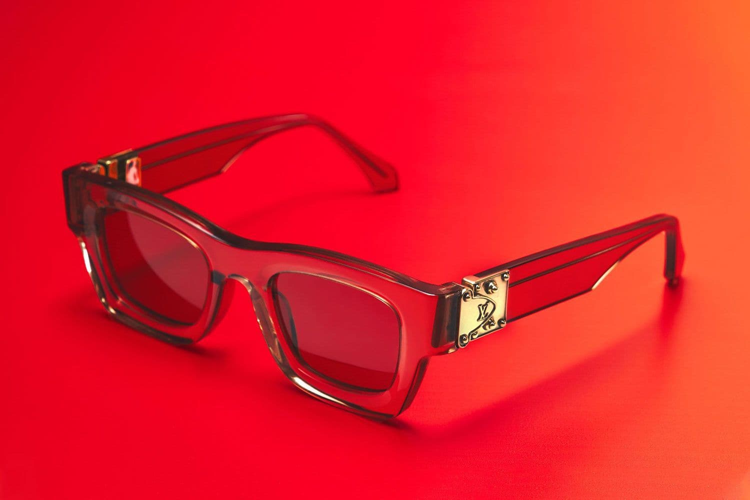 Close-up of red-tinted sunglasses with a Louis Vuitton logo detail on the temple, lit in red.