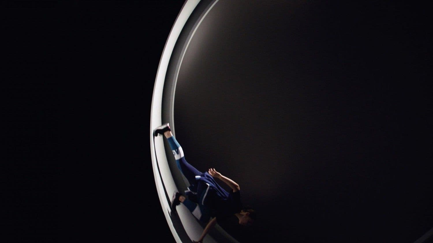 Person in dark clothing running along the curved illuminated wall of the ring set, viewed from above.