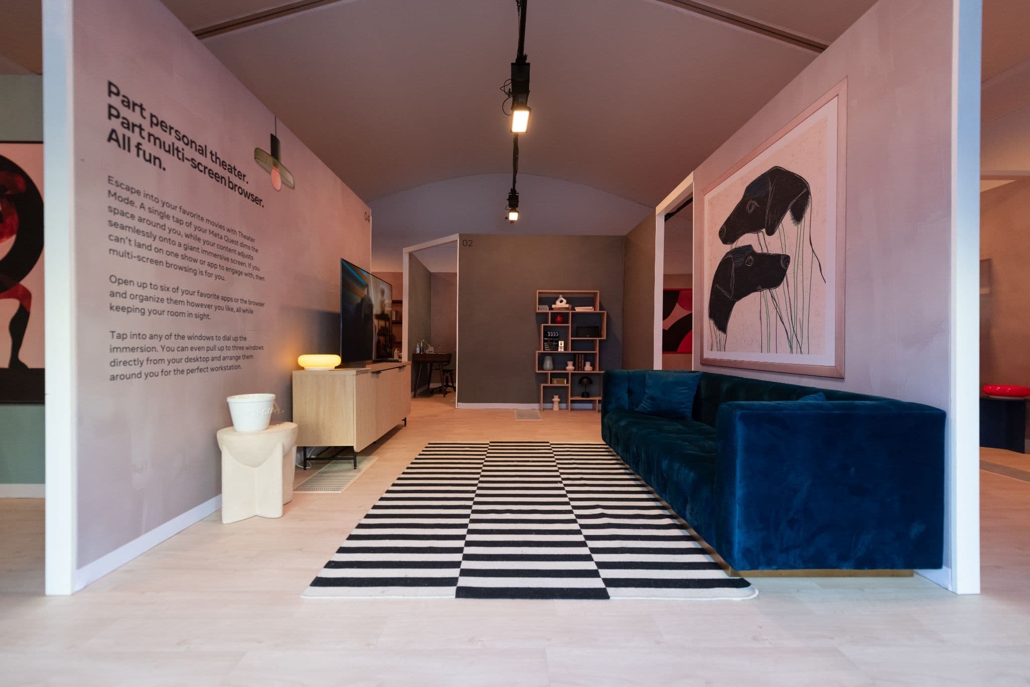 Exhibit room with framed artwork, a teal couch, and a graphic black-and-white rug.