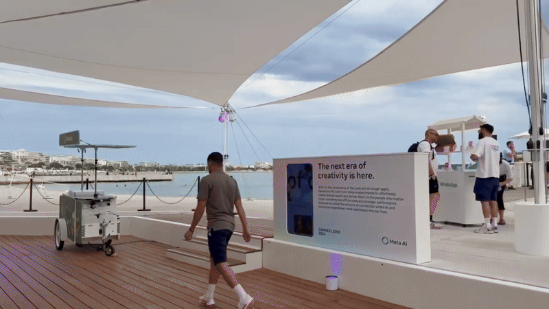 A man walks along a wooden boardwalk under a large sail canopy past a digital sign reading 'The next era of creativity is here.'