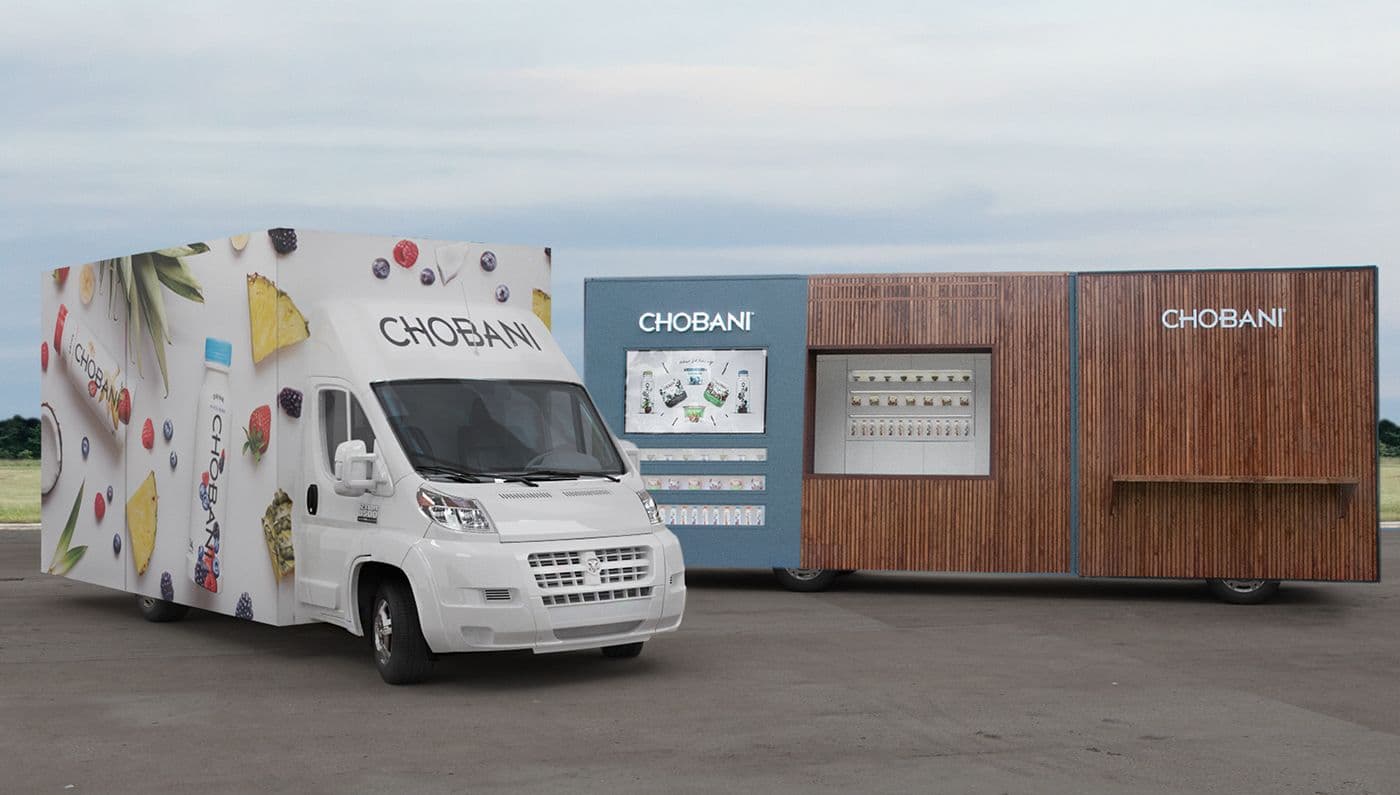 Chobani-branded delivery truck and the wood-slat trailer parked side by side in a lot.