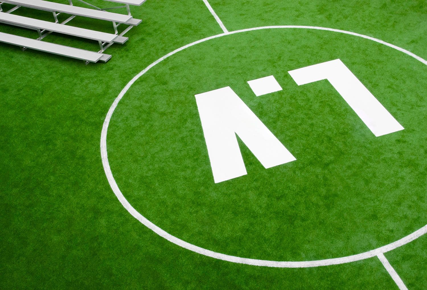 Stacked aluminum spectator bleachers beside a branded number seven marking on the turf pitch.