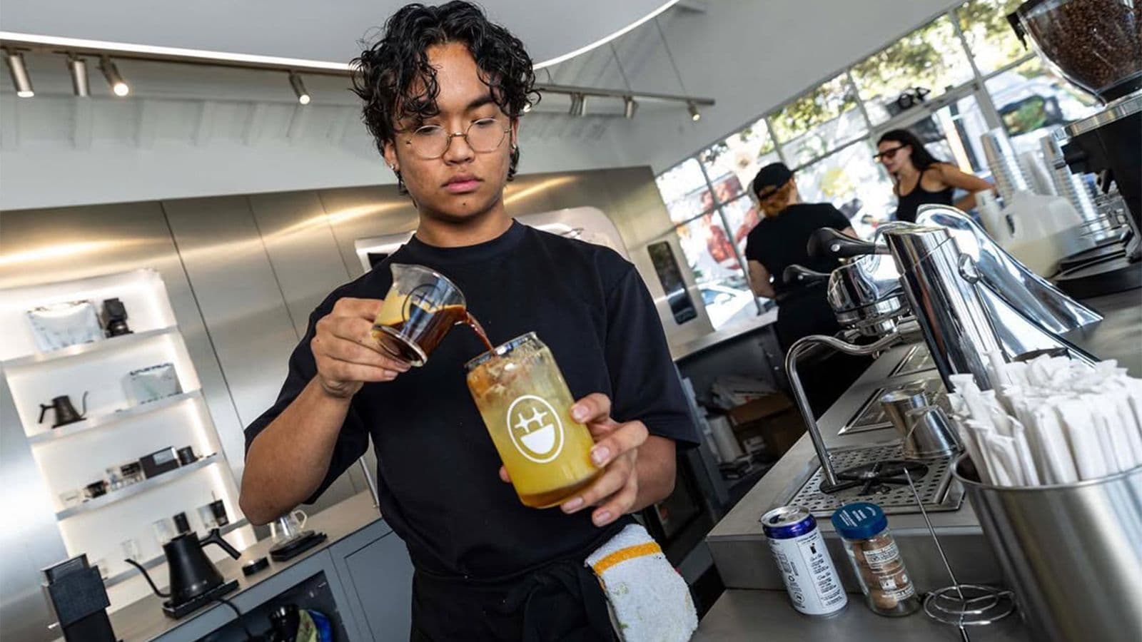 Barista pouring an orange beverage into a cup at an outdoor counter