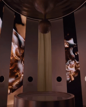 Wide interior view of a dark exhibit room with vertical striped panels surrounding a glowing circular table.