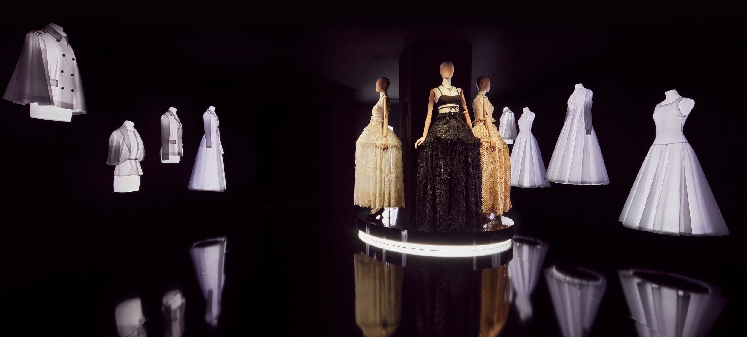 Garments displayed on a rotating illuminated platform in a dark room with a mirrored floor.