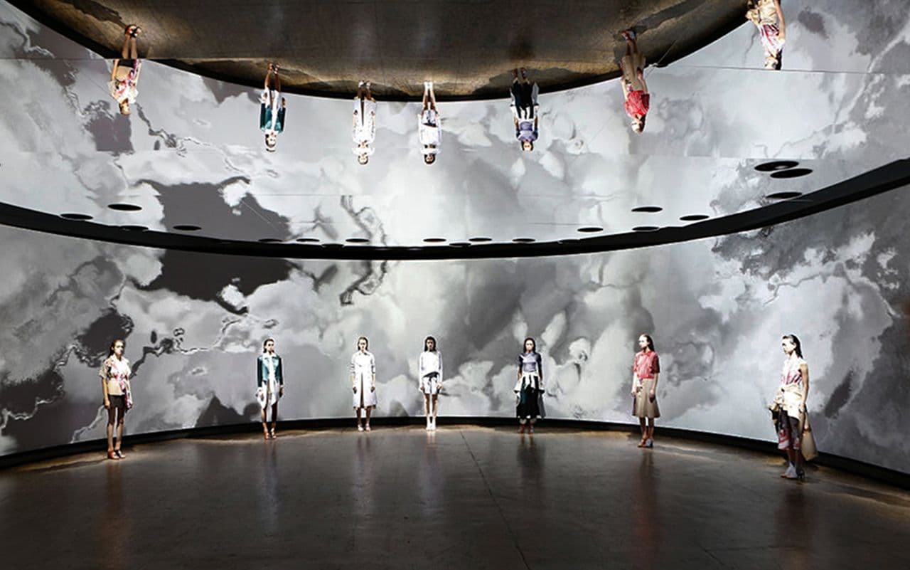 Models standing in a circular runway space with a grayscale marbled cloud pattern projected across the curved walls and ceiling.