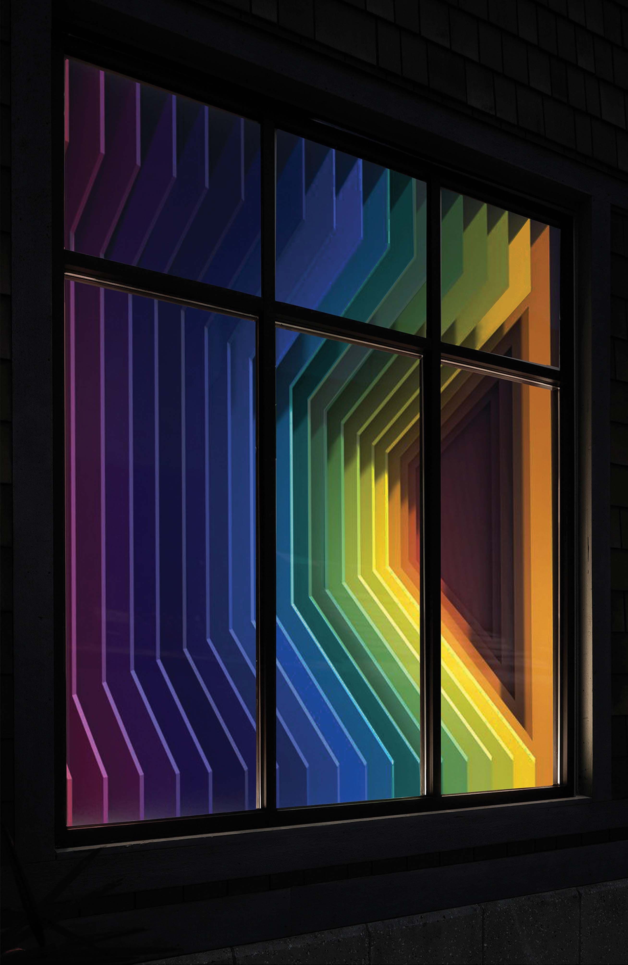 Illuminated window at night showing an angled folded panel installation in a full rainbow gradient.