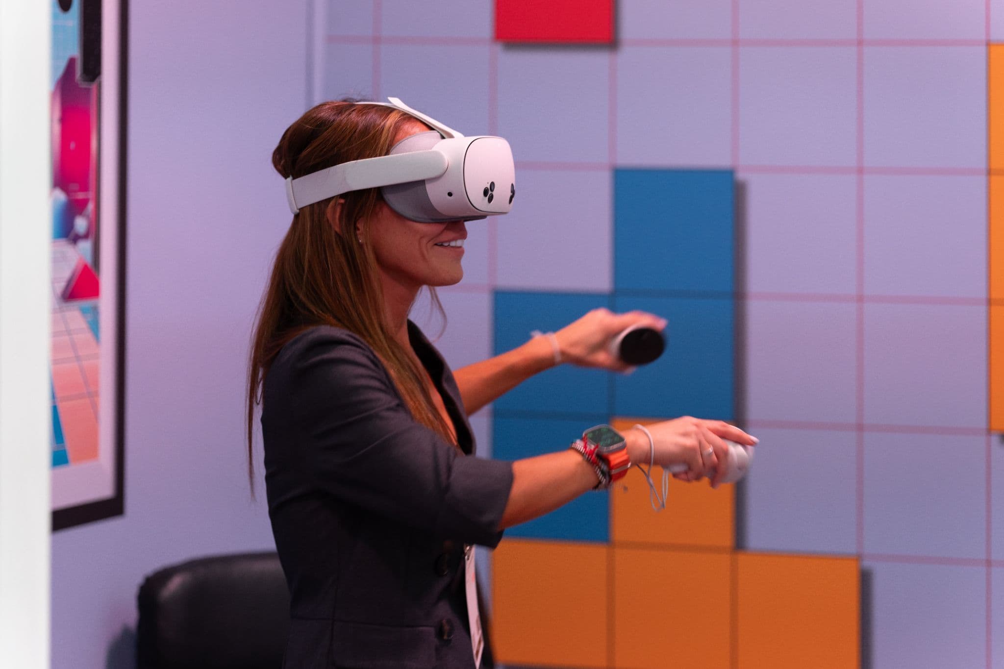 Woman wearing a VR headset and holding controllers in front of a colorful geometric wall.